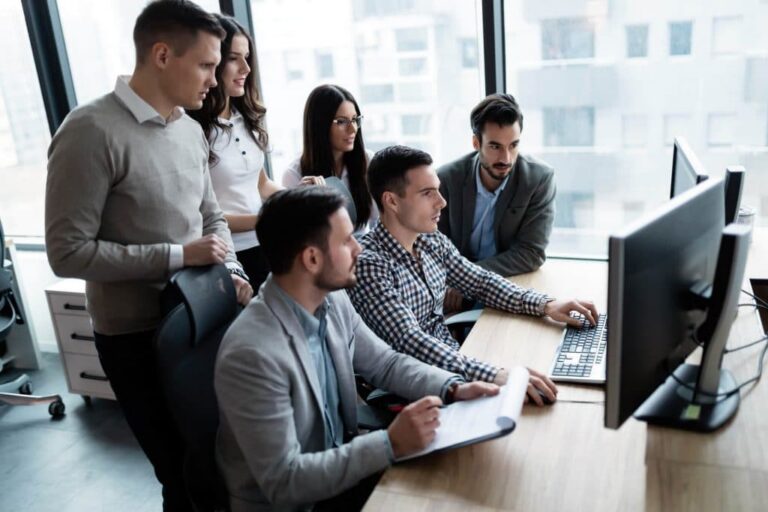 Un grupo de jóvenes profesionales reunidos alrededor de un escritorio, mirando juntos la pantalla de un ordenador en una oficina.