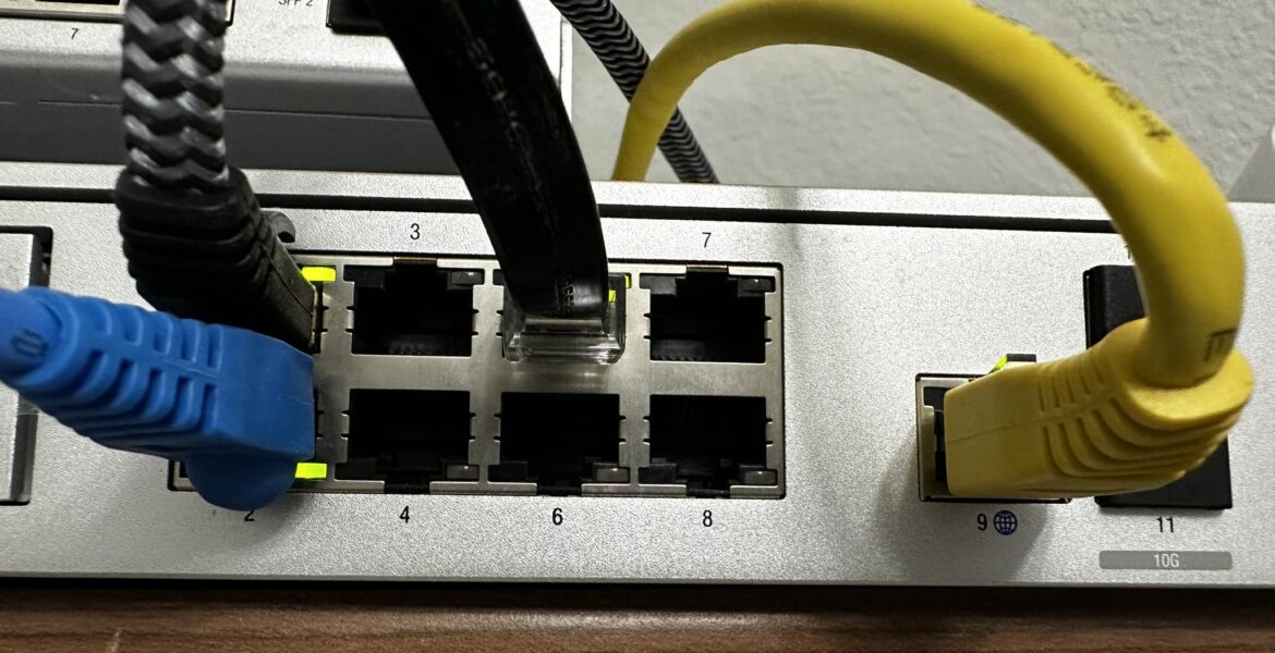 Conmutador de red con cables Ethernet azules y amarillos enchufados en los puertos, mostrando los números de los puertos y los cables en uso.