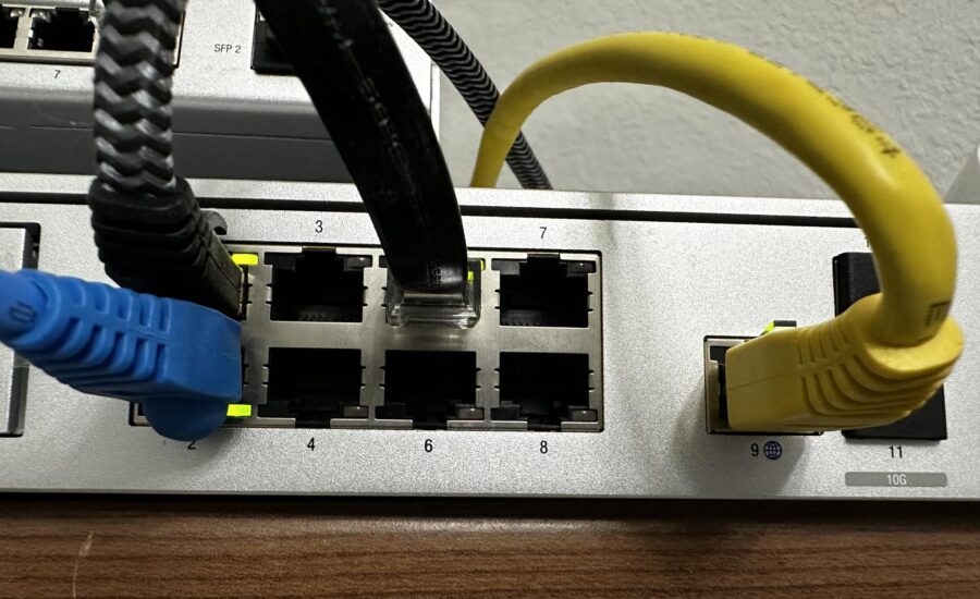 Conmutador de red con cables Ethernet azules y amarillos enchufados en los puertos, mostrando los números de los puertos y los cables en uso.