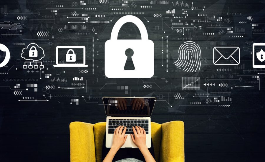 Person typing on a laptop on a yellow chair, with large padlock and digital security icons floating above, illustrating cybersecurity.