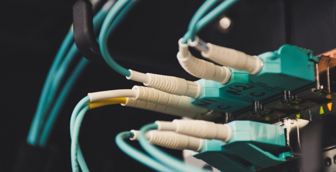 A close-up of teal Ethernet cables plugged into a network patch panel in a server rack, in dim lighting.