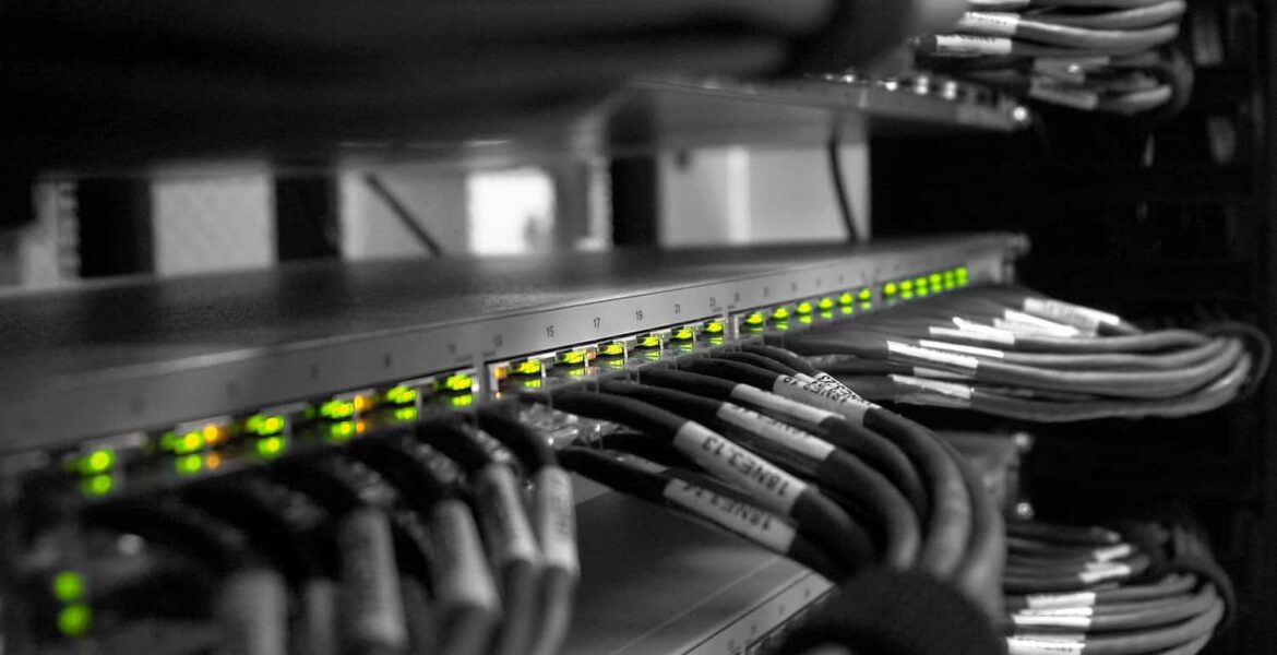 Rack de red con una fila de LED verdes iluminados en un conmutador y cables Ethernet agrupados, etiquetados y organizados en un armario de servidores
