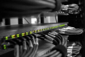 Rack de red con una fila de LED verdes iluminados en un conmutador y cables Ethernet agrupados, etiquetados y organizados en un armario de servidores