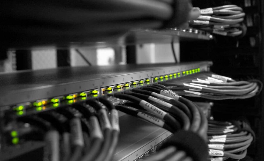 Rack de red con una fila de LED verdes iluminados en un conmutador y cables Ethernet agrupados, etiquetados y organizados en un armario de servidores