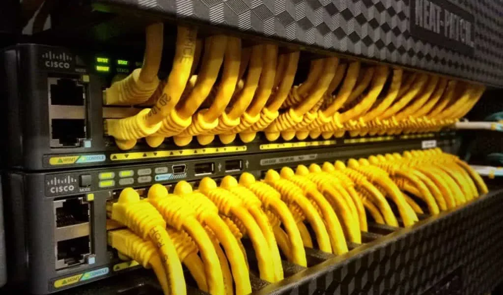 Fila de conmutadores de red de Cisco con numerosos cables Ethernet amarillos conectados.