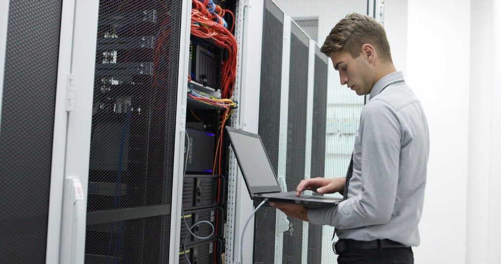 Un technicien informatique utilisant un ordinateur portable pour configurer des serveurs dans la salle de câblage d'un centre de données