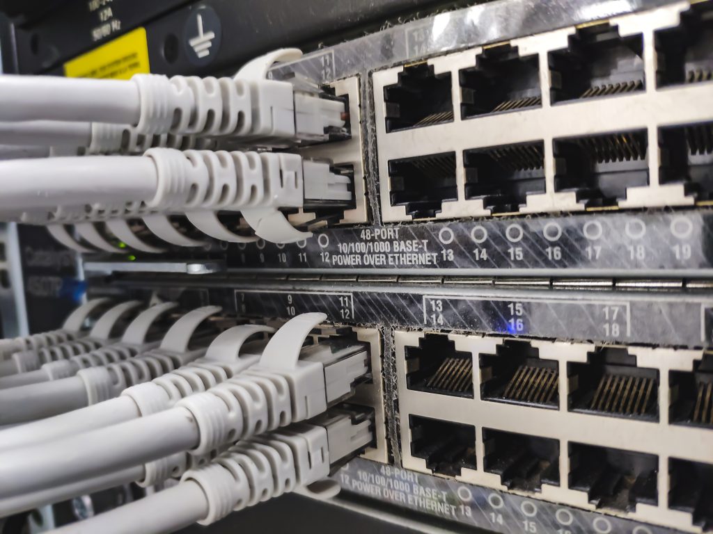Gros plan sur un panneau de raccordement réseau comportant plusieurs ports Ethernet RJ-45 et des câbles gris branchés sur ceux-ci dans une armoire à serveurs, illustrant le câblage de données.