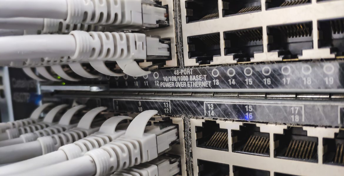Primer plano de un panel de conexiones de red con varios puertos Ethernet RJ-45 y cables grises conectados a ellos en un armario de servidores, en el que se aprecia el cableado de datos.