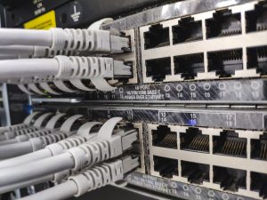 Primer plano de un panel de conexiones de red con varios puertos Ethernet RJ-45 y cables grises conectados a ellos en un armario de servidores, en el que se aprecia el cableado de datos.