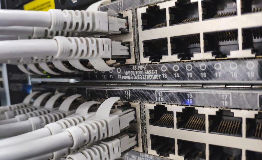Close-up of a network patch panel with multiple RJ-45 Ethernet ports and gray cables plugged into them in a server rack, showing data cabling.